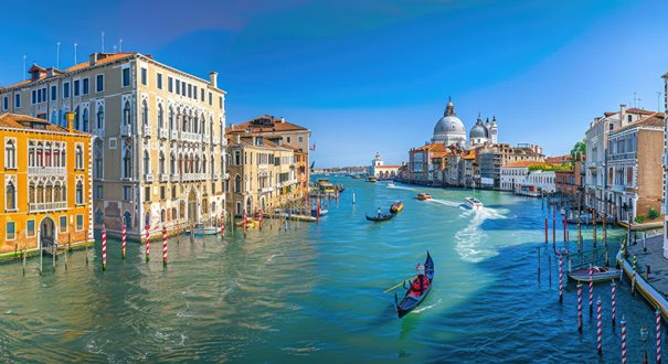 A man is riding a gondola down a calm canal in Venice, Italy