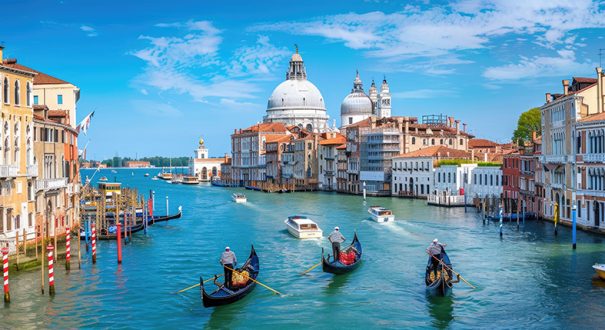 A man is riding a gondola down a calm canal in Venice, Italy