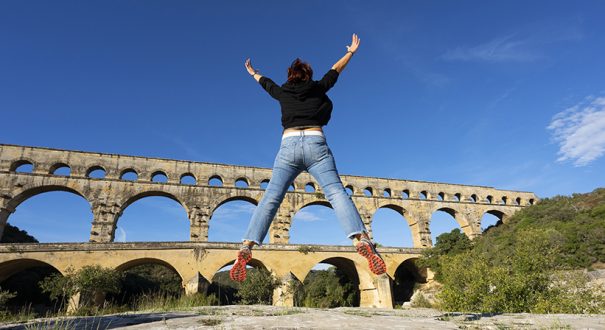 Woman jumping in front of Pont du Gard, France