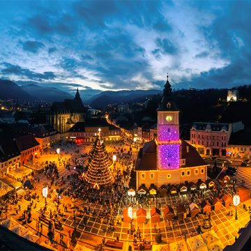 Aerial drone wide view of The Council Square at dusk in Brasov, Romania. Old city centre decorated for Christmas. County Museum of History, buildings, people